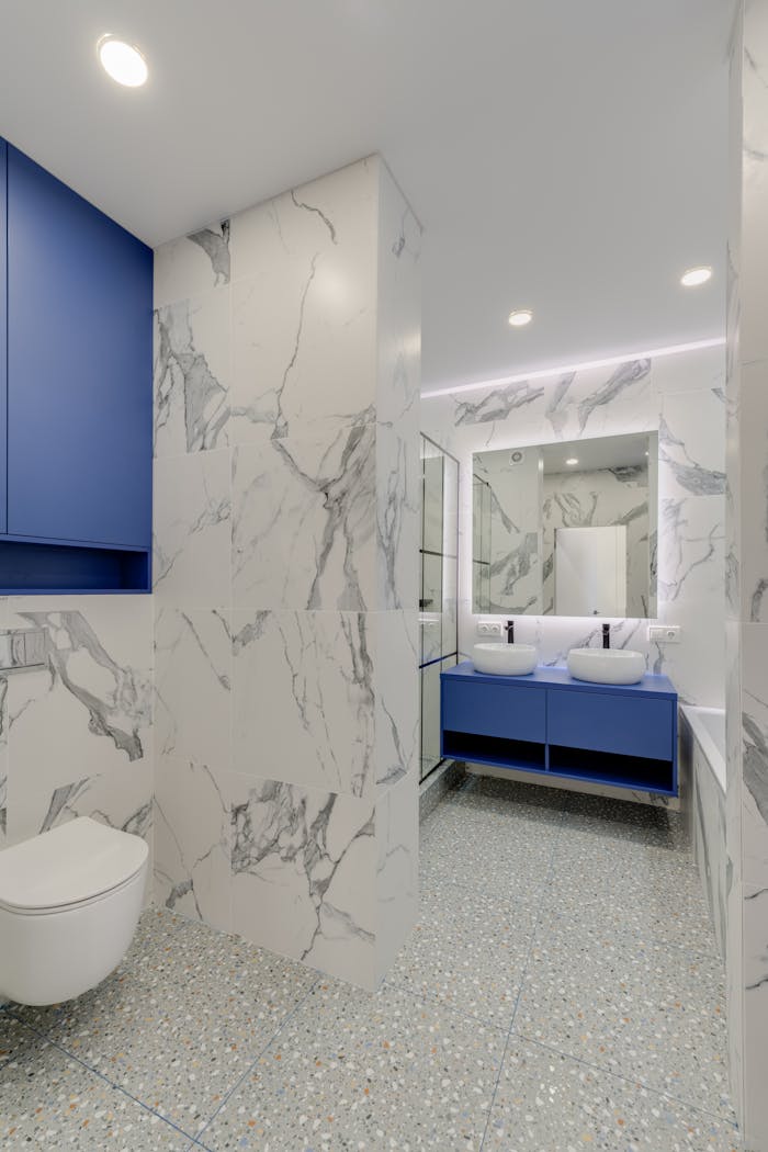 Services-03 Elegant bathroom featuring blue cabinetry, marble walls, and twin sinks for a luxurious feel.