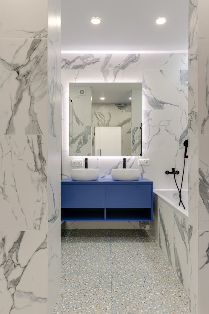 why-choose-us Stylish marble bathroom with blue vanity and double sinks.