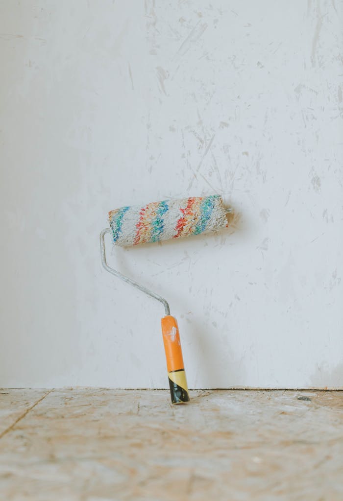 digital A vivid paint roller rests against a textured white wall on a wooden floor, perfect for renovation themes.