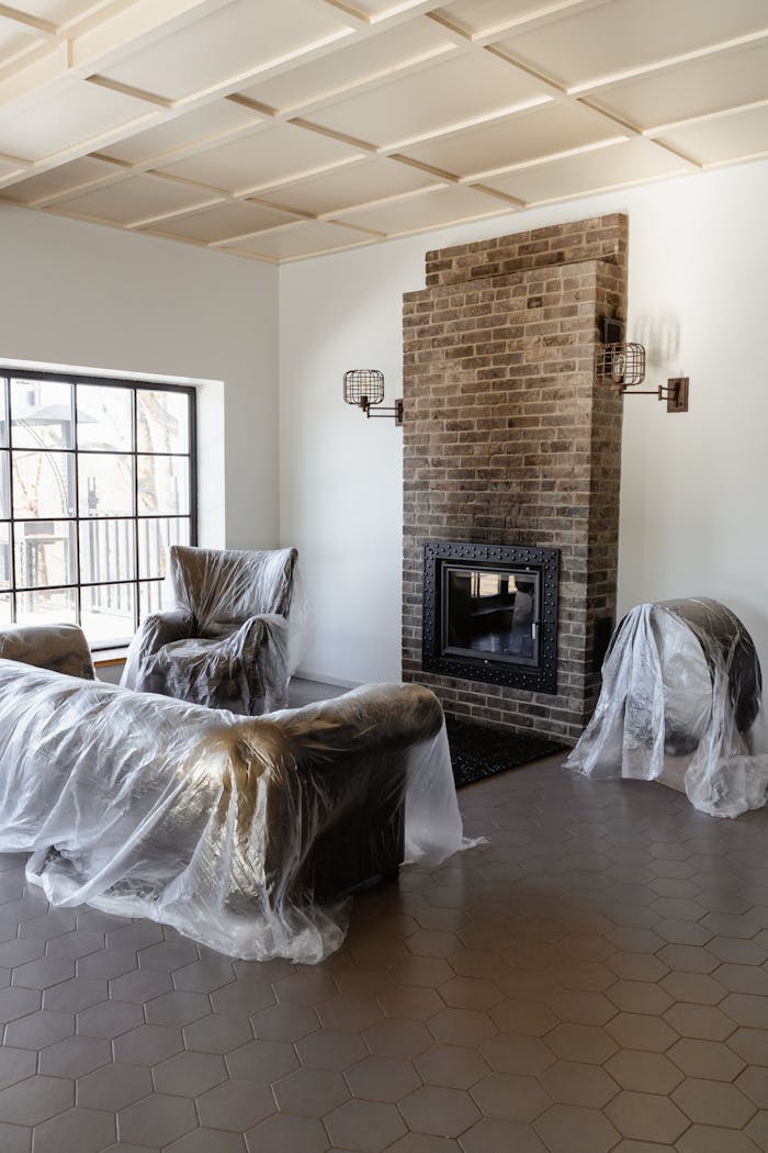 creative-02 A cozy, modern living room with plastic-covered furniture and a brick fireplace under renovation.